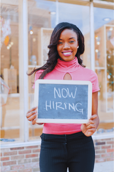 Small business owner holding a now hiring sign outside her workplace